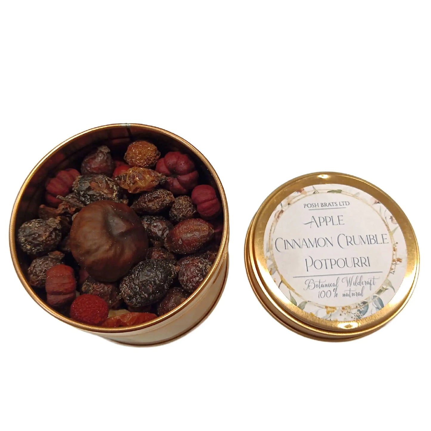 Open a tin of Posh Brats Wildcraft Botanical Potpourri in Apple Cinnamon Crumble scent, featuring assorted dried botanicals like pinecones, herbs, and spherical seeds, with a lid adorned with the same label and floral accents.