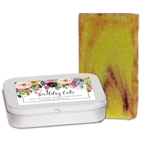 A floral-designed tin labeled Birthday Cake Sugar Scrub Bar from Posh Brats holds a yellow vegan scrub bar with red marbled streaks, perfect for an exfoliating shower experience.