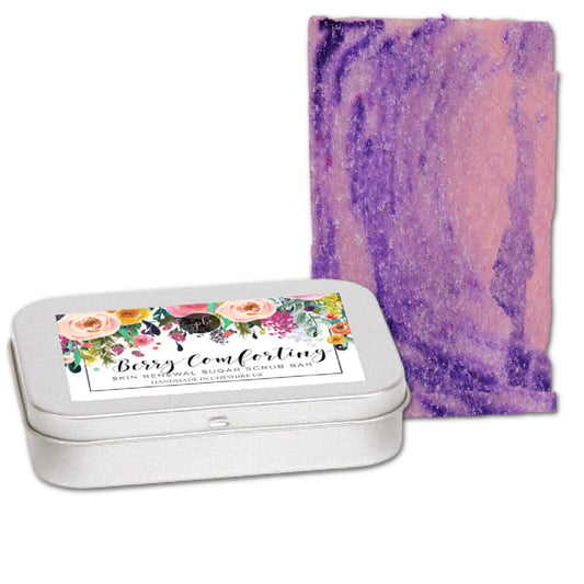 A tin labeled Berry Comforting Sugar Scrub Bar by Posh Brats sits next to an exfoliating bar with a marbled pink-purple design, offering a vegan scrub for silky-smooth, rejuvenated skin.
