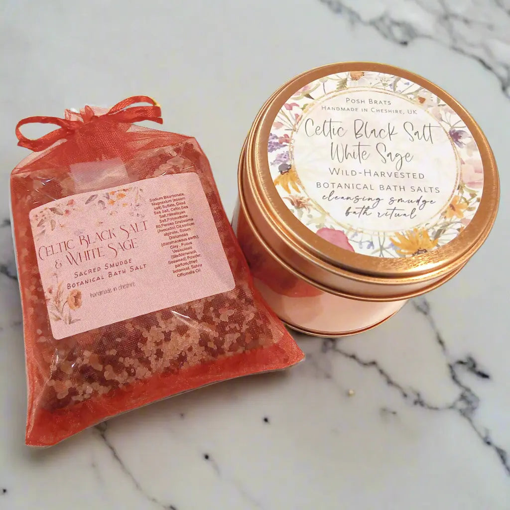 A package of Posh Brats’ Celtic Black Salt White Sage Smudge Bath Salt in a pink organza bag sits beside a matching floral tin. These wild-harvested botanical salts provide cleansing and purification for a relaxing soak.