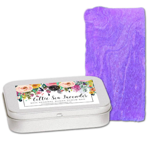 A purple scrub bar sits next to an open silver tin with a floral label reading Celtic Sea Lavender Sugar Scrub Bar, crafted by Posh Brats using organic sugar crystals for rejuvenation.