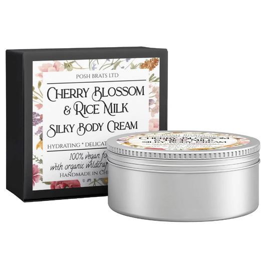 A tin of Cherry Blossom + Rice Milk Silky Body Butter Cream by Posh Brats is displayed with its floral-decorated box, highlighting its hydrating, delicate, vegan qualities and handmade nature with organic wildcrafted oils.