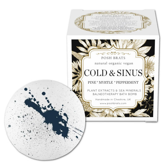 A white bath bomb with black speckles, labeled Posh Brats Cold Sinus Aromatherapy, showcases pine, myrtle, and peppermint oils. The decorative box highlights natural, organic, vegan ingredients designed to ease sinus congestion. Made in Cheshire, UK by Posh Brats.