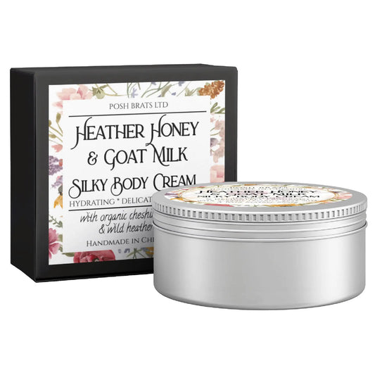Posh Brats Heather Honey + Goat Milk Silky Body Butter Cream, in a round silver tin with a floral label, sits before its matching black and white box. The packaging emphasizes organic chestnut and wild heather essences.