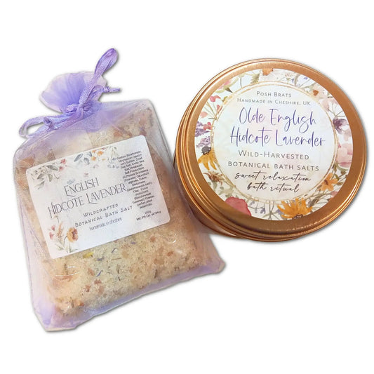 A purple organza bag with English Hidcote Lavender Botanical Bath Salt is beside a floral tin labeled Olde English Hidcote Lavender. Both products by Posh Brats offer a spa-like relaxation experience.