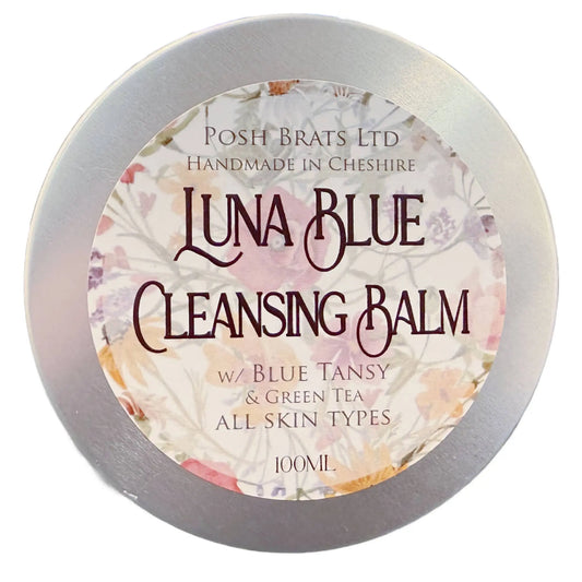 The image shows a 100ml round tin with a metallic lid labeled Luna Blue Tansy Cleansing Balm by Posh Brats. Handmade in Cheshire, it combines blue tansy oil and green tea for radiant skin, suitable for all skin types.