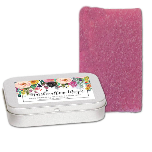 A pink, rectangular Marshmallow Magic Sugar Scrub Bar by Posh Brats sits beside an open silver tin with a vibrant floral label, promising a delightful and enchanting exfoliation experience.
