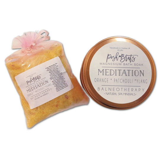 A package and container of Posh Brats Meditation Aromatherapy Bath Salt. The left package contains orange crystals with essential oils, while the round container on the right features scents such as orange, patchouli, and ylang atop Himalayan pink salt.