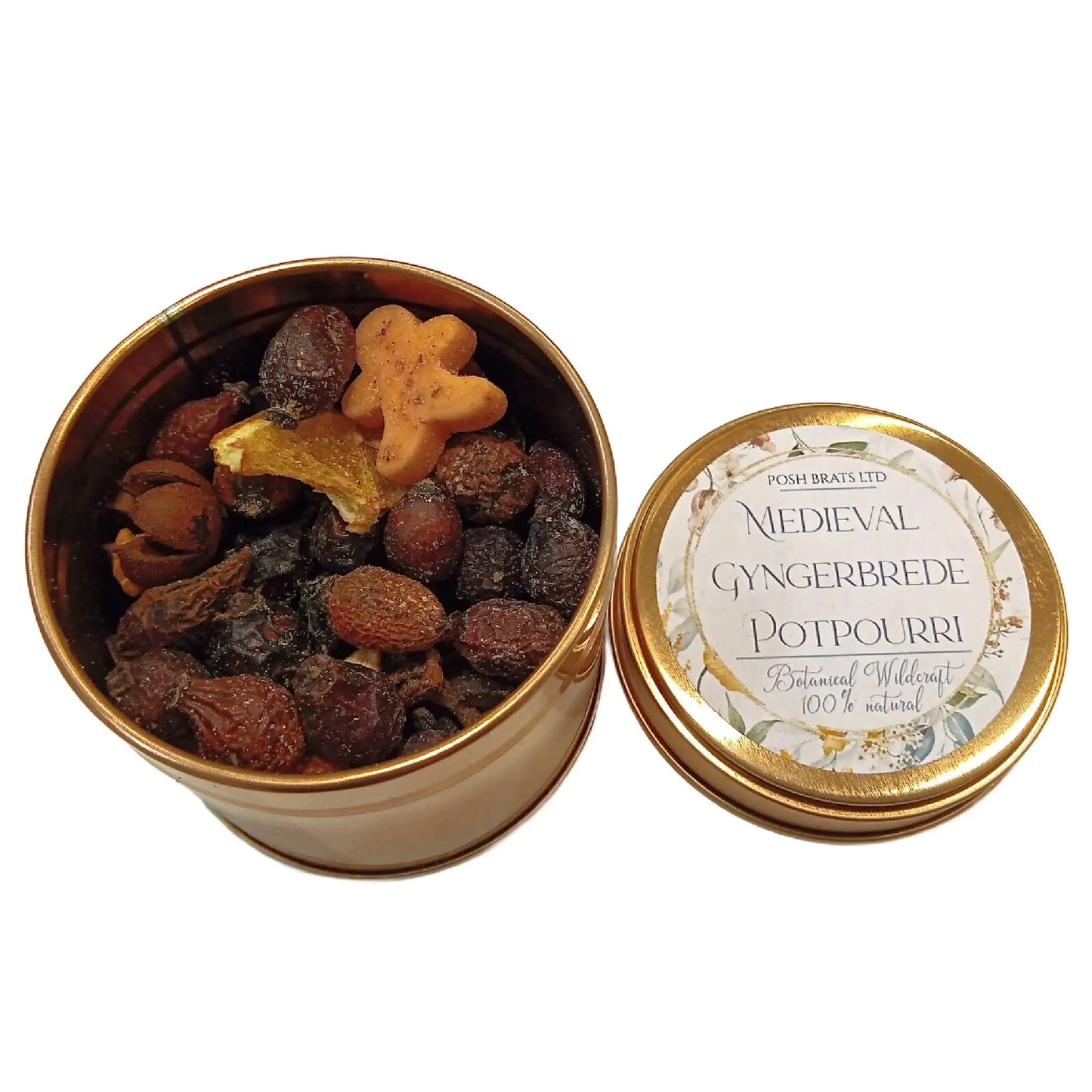 An open tin labeled Wildcraft Botanical Potpourri by Posh Brats reveals a blend of dried fruits and spices, topped with a small gingerbread-shaped piece, as the lid rests beside the tin.