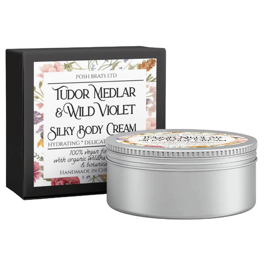 The Tudor Medlar & Wild Violet Silky Body Butter Cream by Posh Brats is in a round silver jar with a floral label, accompanied by a matching design box containing detailed product info.