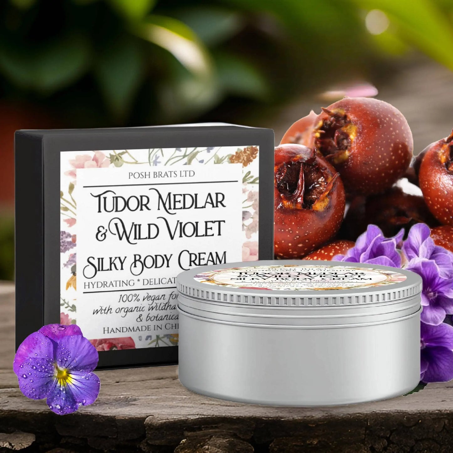 A decorative tin of Posh Brats Tudor Medlar & Wild Violet Silky Body Butter Cream is displayed against floral-themed packaging, surrounded by fresh medlar fruits and vibrant violets, exuding a natural, luxurious vibe.