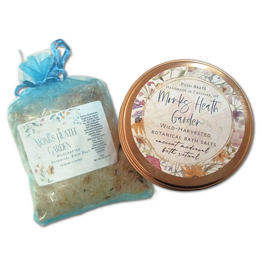 A packet and tin of Posh Brats Monks Heath Garden Medieval Botanical Bath Salt. The blue mesh bag contains the packet, while the tin has a floral lid. Elegant labels describe calming ingredients like rosemary and lavender, offering relaxation with each use.