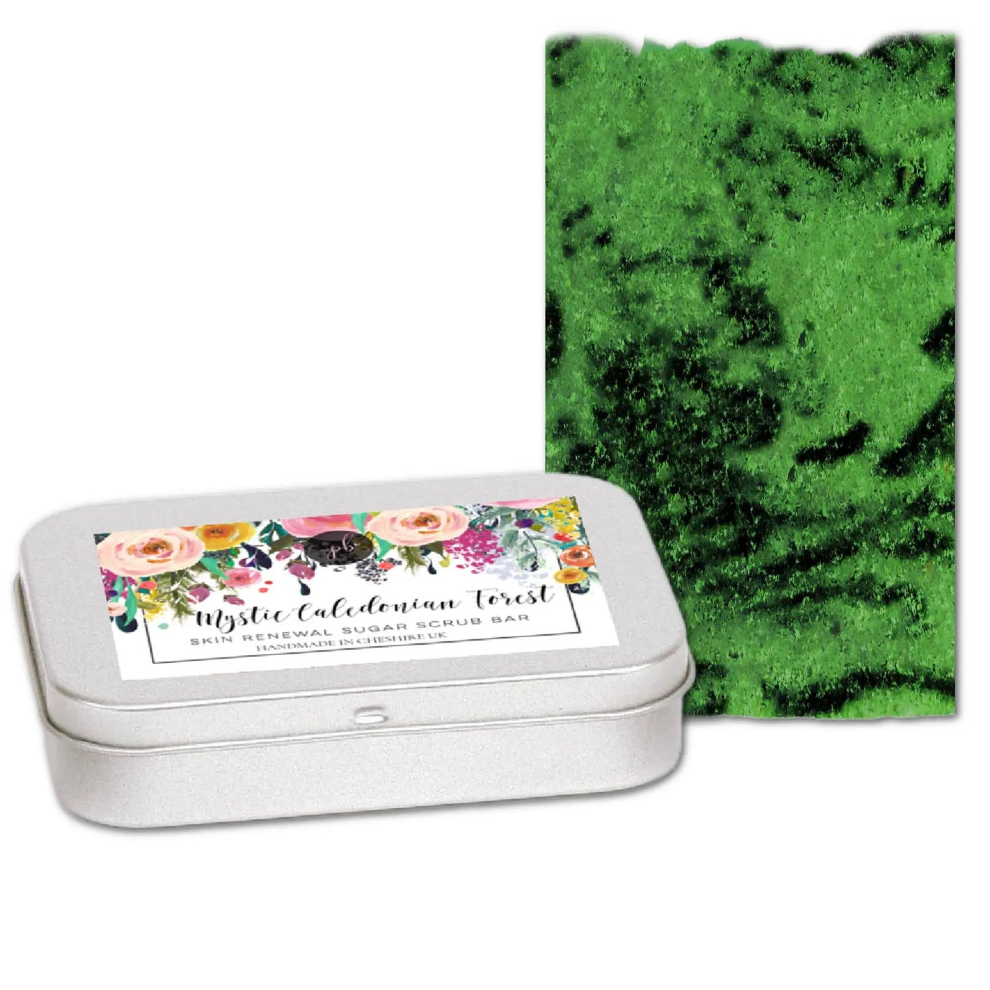 A white tin labeled Mystic Caledonian Forest Sugar Scrub Bar by Posh Brats, adorned with a floral design and infused with Scottish botanicals, sits next to a green textured scrub bar resembling lush foliage, capturing the essence of an enchanted forest.