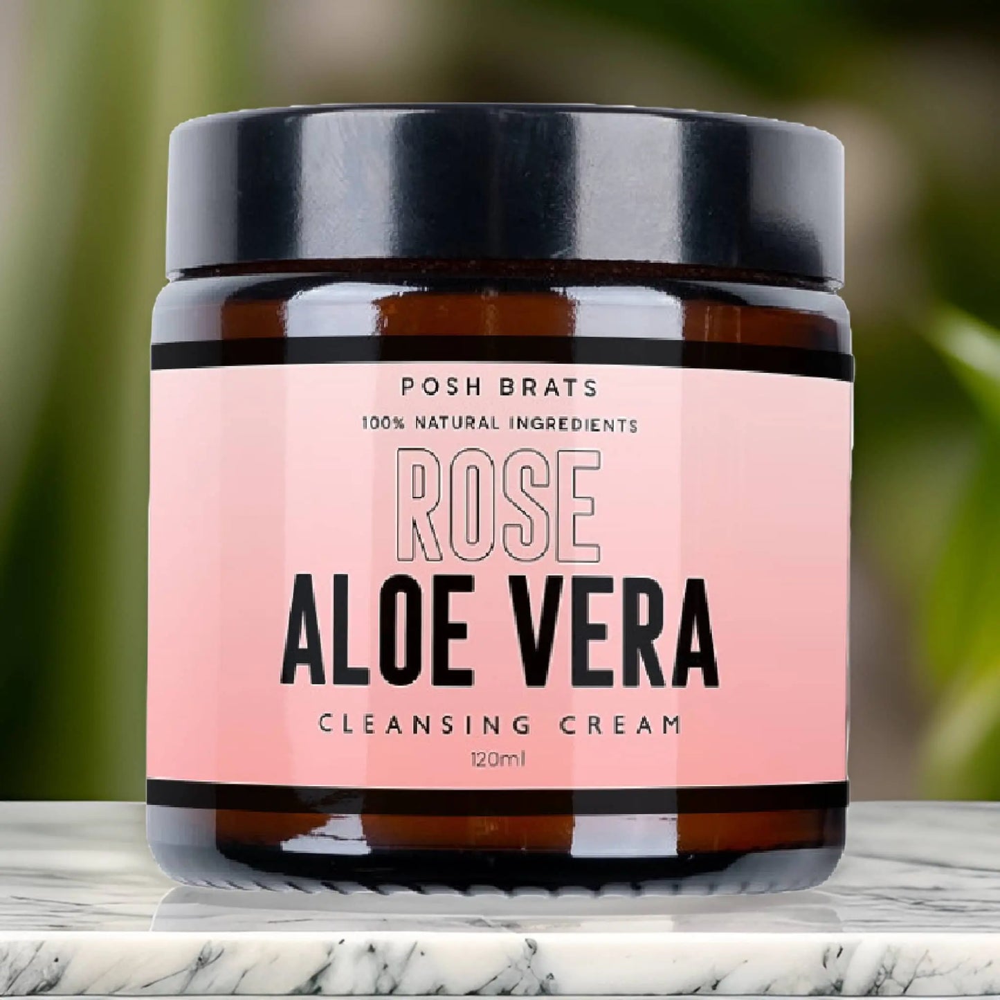 The Posh Brats Rose Aloe Vera Cleansing Cream, with a soothing aloe vera extract, is available in a 120 ml jar with a black lid. Its pink label with black and white text stands out on marble, against a soothing green blurred backdrop.
