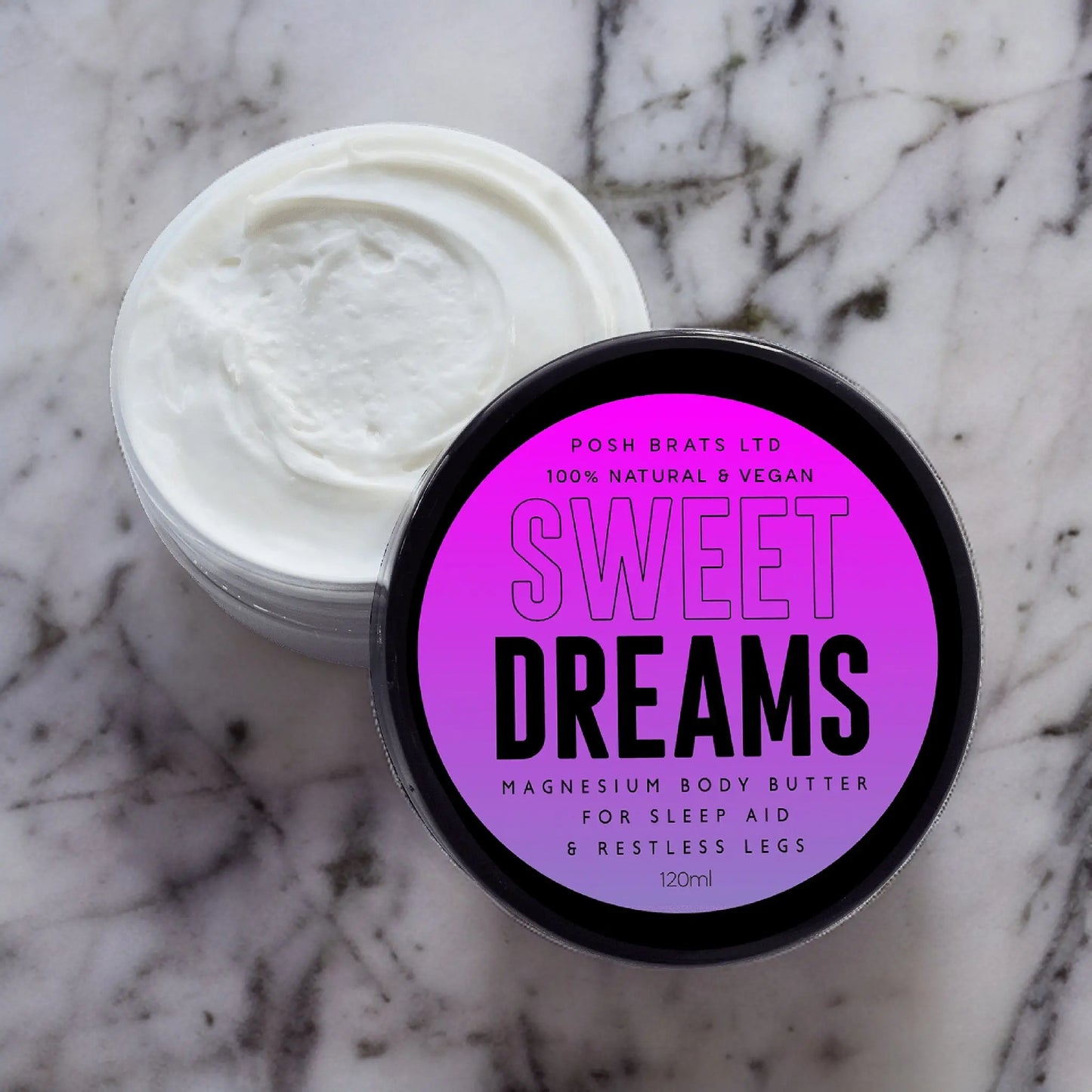 An open jar of Posh Brats Sweet Dreams Magnesium Body Butter sits on a marble surface. Its black and purple label indicates its natural, vegan, and promotes relaxation, deep sleep, and aids in better sleep for restless legs.