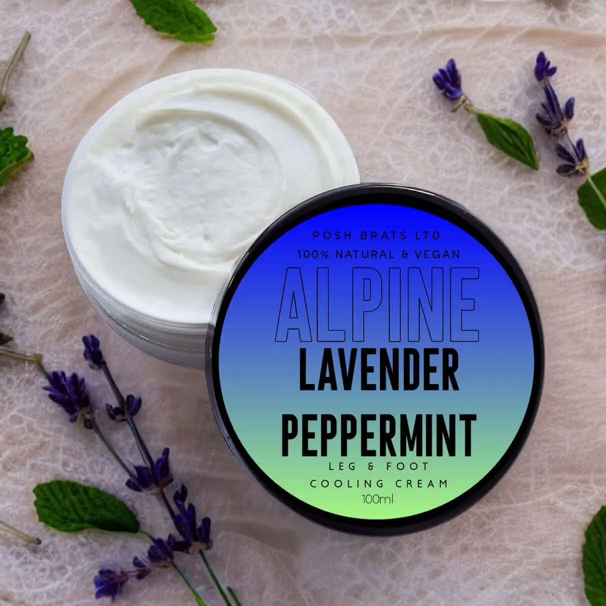 A jar of Posh Brats Alpine Lavender Peppermint Leg + Foot Cream lies on a textured surface, surrounded by lavender and mint. This luxurious cream is white and smooth, ideal for soothing cracked heels.