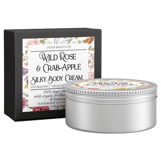 A silver tin of Posh Brats Wild Rose & Crab Apple Silky Body Butter Cream is displayed next to its sleek black box, featuring a floral design that highlights its vegan formula, organic ingredients, and handmade origin.