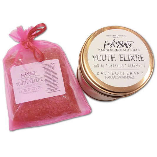 A pink drawstring bag holds Posh Brats Youth Elixre Magnesium Aromatherapy Bath Salt, infused with essential oils of santal, geranium, and grapefruit. It features Dead Sea salt for a natural spa experience and is complemented by a matching tin lid.