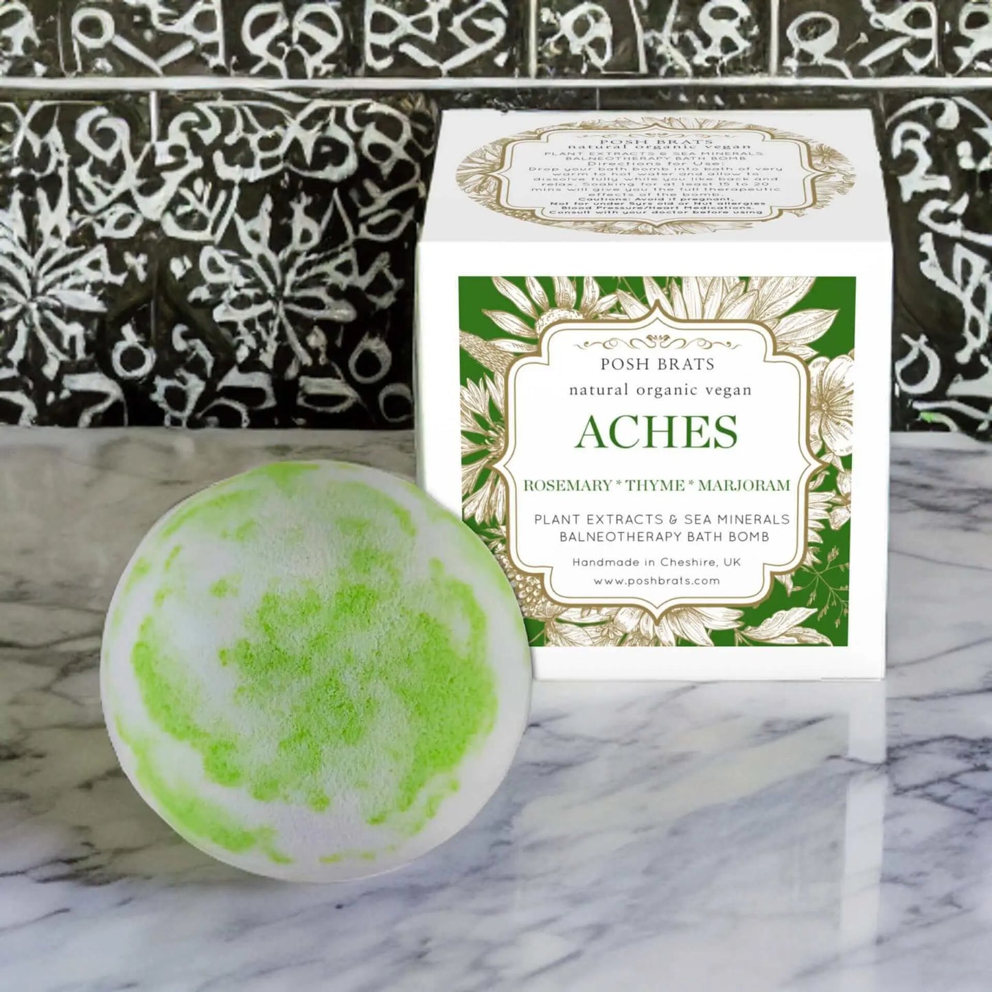 A green and white Aches Aromatherapy Bath Bomb from Posh Brats sits before a box labeled natural organic vegan ACHES. The packaging emphasizes rosemary, thyme, marjoram, essential oils, plant extracts, and sea minerals for muscle relief in a balneotherapy bath.