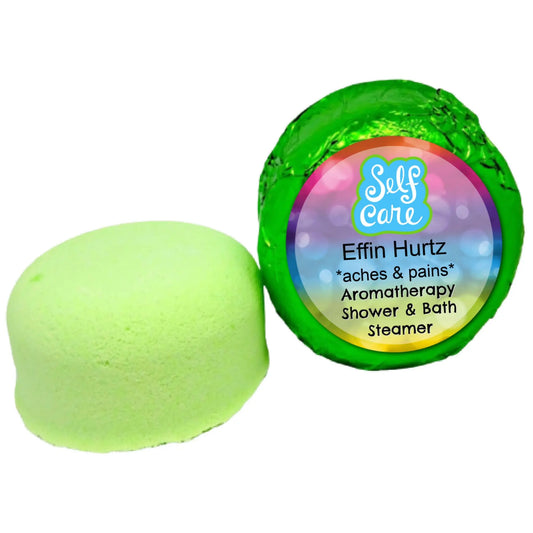 A light green Posh Brats Effin Hurtz Aromatherapy Shower Steamer is featured. One is unwrapped, showcasing its soothing essential oils blend, while the other remains wrapped in shiny green foil. The label reads Self Care, Effin Hurtz, *aches & pains*, Aromatherapy Shower & Bath Steamer.