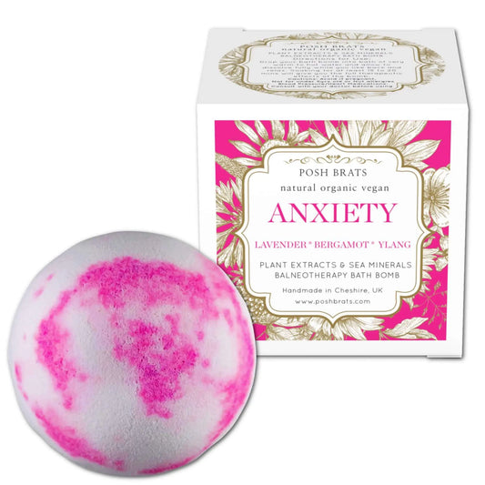A pink and white swirled bath bomb rests by its floral-themed box labeled: Posh Brats Anxiety Aromatherapy Bath Bomb. This vegan, natural, organic product offers relaxing Lavender, Bergamot, and Ylang scents.