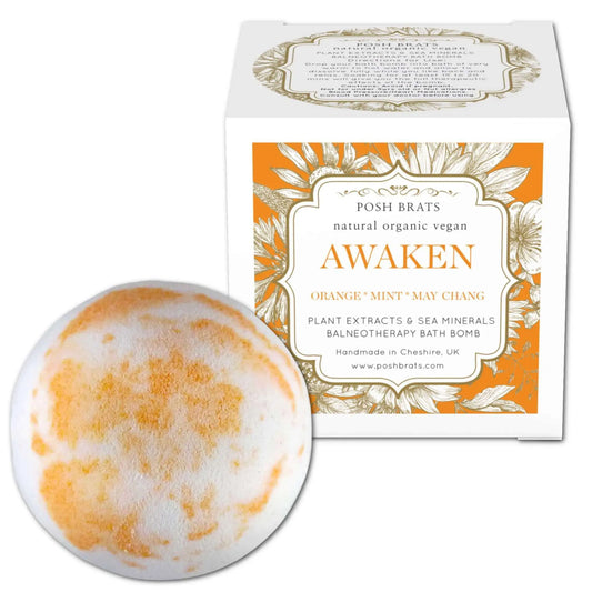 The Awaken Aromatherapy Bath Bomb by Posh Brats, with an orange and white marbled design, rests beside its matching box. Infused with Orange, Mint, May Chang essential oils, plant extracts, and sea minerals, it offers a rejuvenating bath experience.