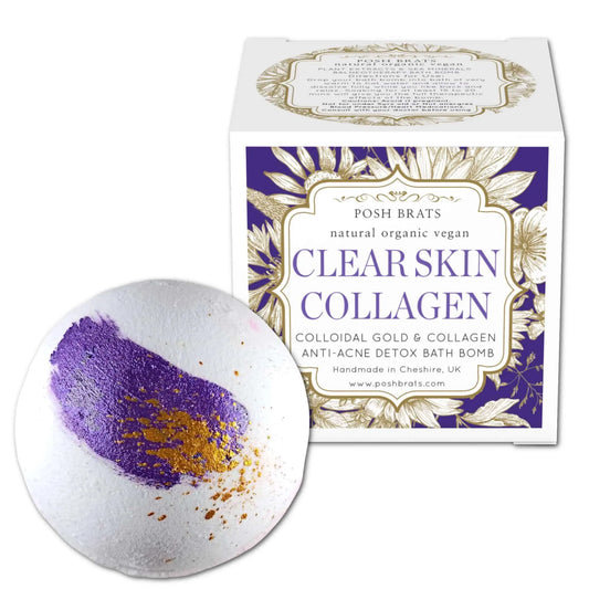 A round Clear Skin Collagen Bath Bomb with purple and gold colors sits by a white and purple box labeled Posh Brats. This organic, vegan product contains colloidal gold and collagen for radiant skin.