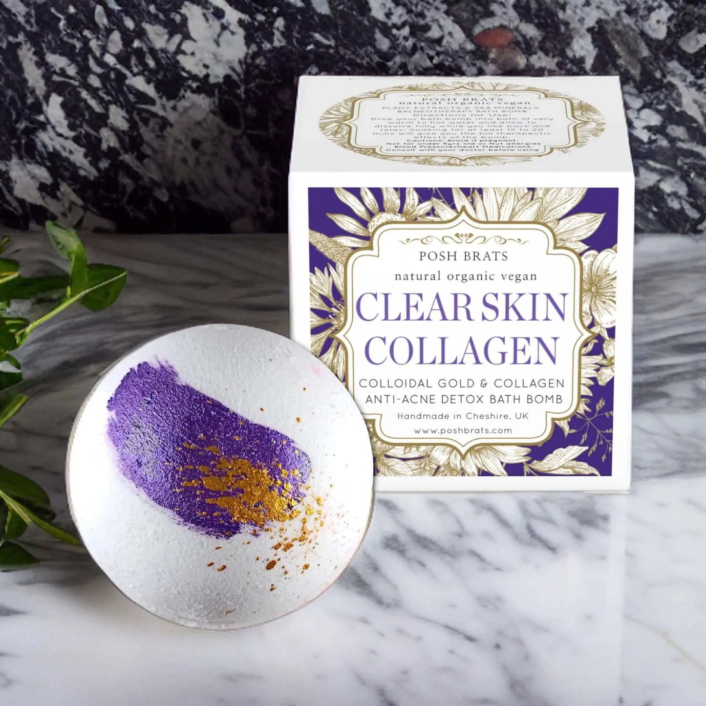 A purple and gold Clear Skin Collagen Bath Bomb from Posh Brats sits on a marble surface next to a box promoting its natural, organic, vegan ingredients aimed at an anti-acne detox. A plant leaf peeks out, symbolizing radiant skin.