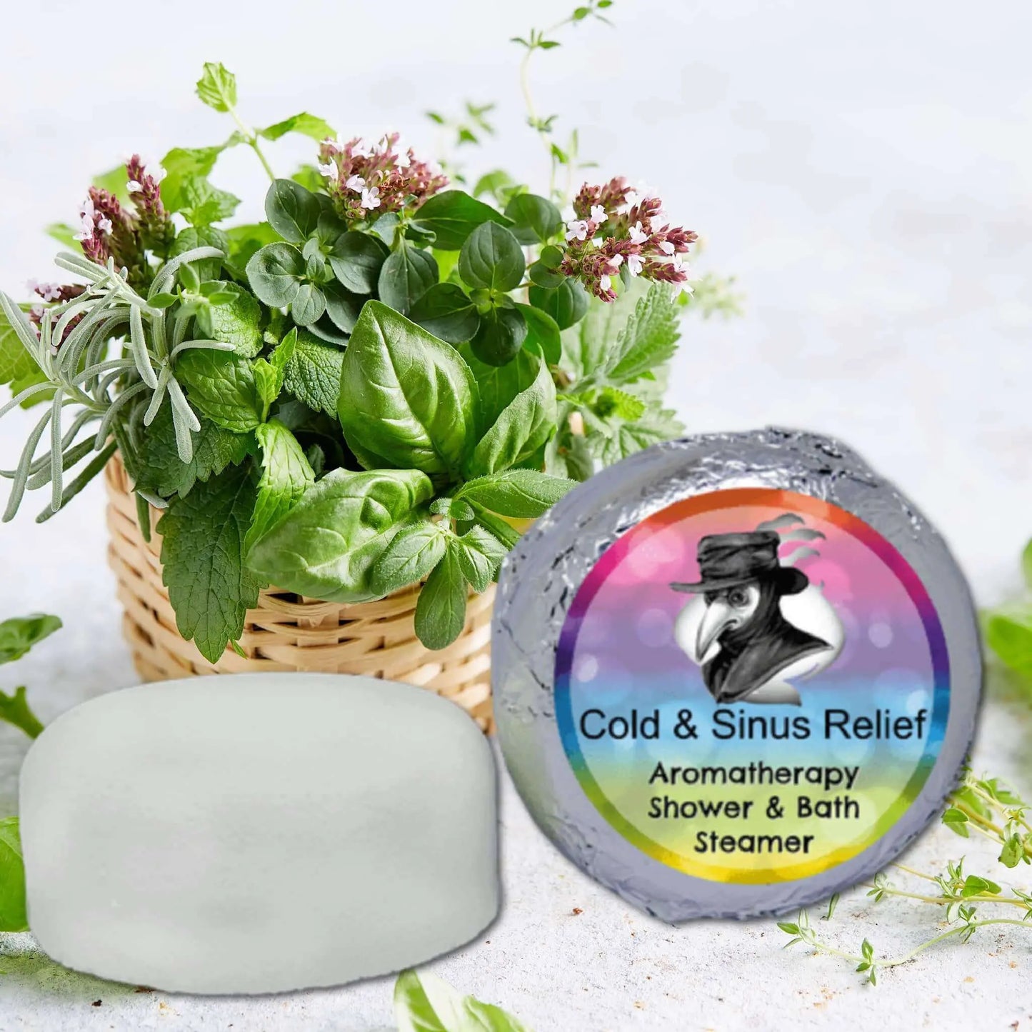 Aromatherapy herbs in a basket enhance the Cold Sinus Aromatherapy Shower Steamer by Posh Brats, featuring a bird with a hat on its package, promising congestion relief against softly blurred greenery.