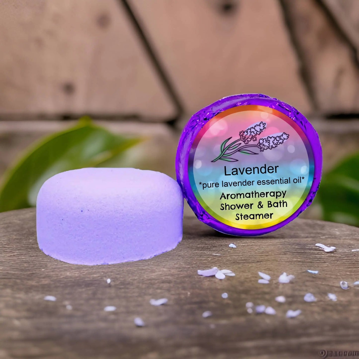 Posh Brats Lavender Aromatherapy Shower Steamer rests on a wooden surface, its colorful package adorned with lavender illustrations. The text Lavender: Pure essential oil, Aromatherapy Shower & Bath Steamer is surrounded by scattered lavender petals, evoking a calming scent.