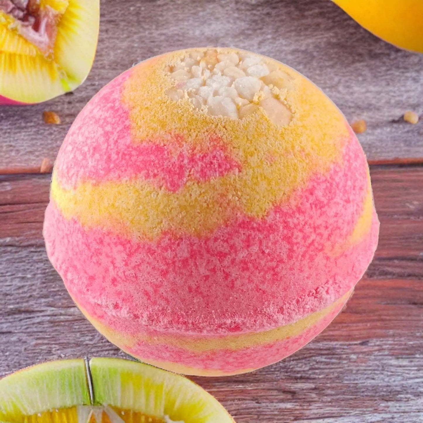 A Mango Margarita Fizzy Bath Bomb from Posh Brats, swirled with pink and yellow hues, lies on a wooden surface surrounded by sliced fruit, creating a vibrant Tropical Paradise atmosphere.