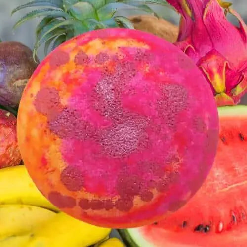 A vibrant image features a pink and orange dragon fruit, surrounded by tropical delights like bananas, watermelon, and a whole dragon fruit—capturing the fruity essence of a Monkey Farts Fizzy Bath Bomb by Posh Brats.