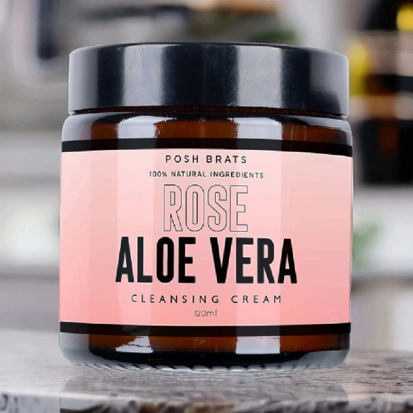 The Rose Aloe Vera Cleansing Cream by Posh Brats shines in pink with black and white text, emphasizing its 100% natural aloe vera extract and rose oil. The 120 ml jar stands against a softly blurred background.