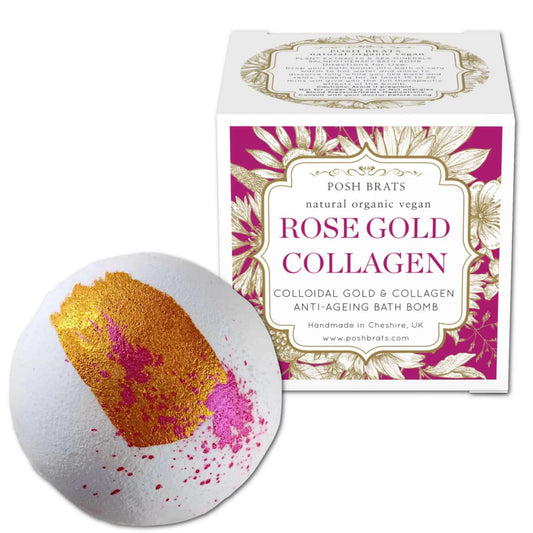 A white bath bomb with pink and gold splashes lies next to a Posh Brats Rose Gold Collagen box. Embellished with ornate gold leaf, it offers a natural, organic, vegan anti-aging journey. Indulge in the Posh Brats Rose Gold Collagen Aromatherapy Bath Bomb for a revitalizing experience.