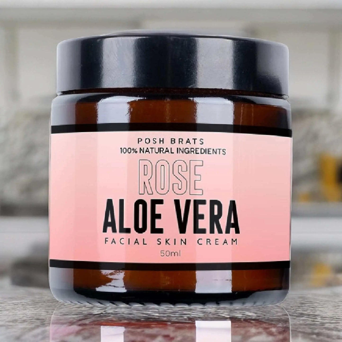The Rose Aloe Vera Skin Cream by Posh Brats, in a jar with a black lid and pink-black label stating 100% Natural Ingredients and 50ml, is known for anti-inflammatory properties that promise radiant skin. The jar displays elegantly on a reflective surface.