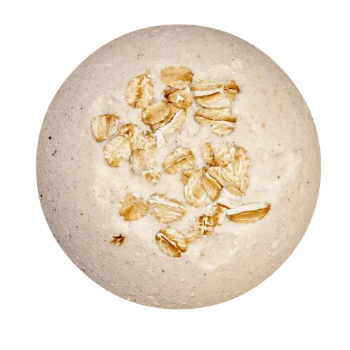 The Posh Brats Skin Soothing Milk Oats Unscented Fizzy Bath Bomb is round, light beige, and has embedded oats on its surface, promising a soothing skin experience.
