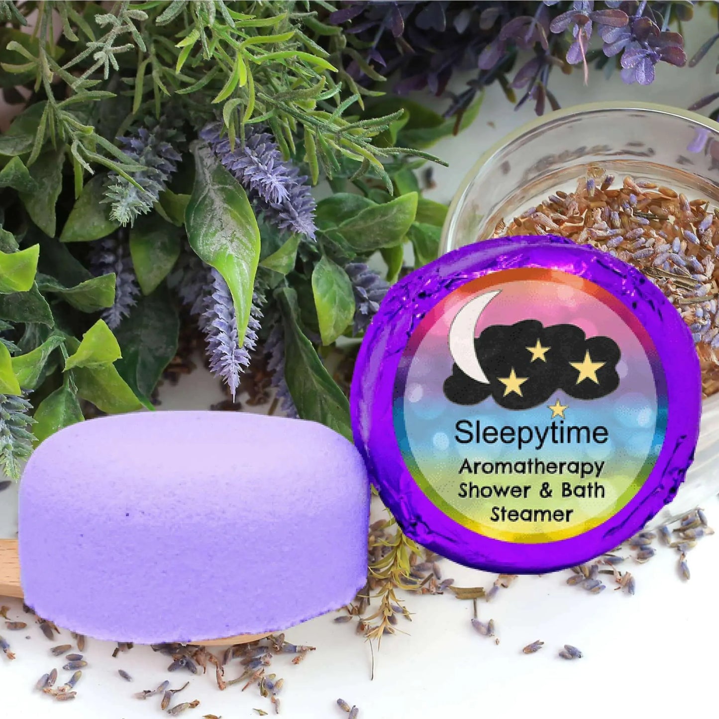 A purple Sleepytime Aromatherapy Shower Steamer by Posh Brats, infused with natural essential oils, sits on wood amid lavender and leaves. In the background, dried lavender enhances the scene, with its label featuring moon and star graphics.