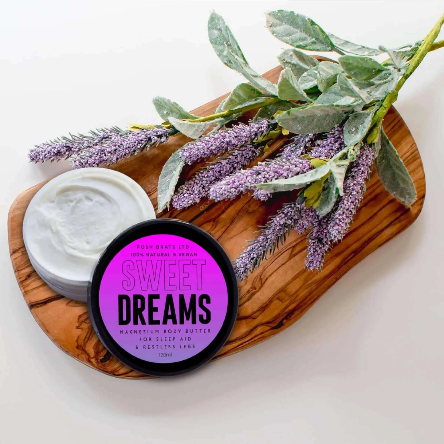 A jar of Posh Brats Sweet Dreams Magnesium Body Butter sits on a wooden board with lavender, offering vegan, creamy white comfort for relaxation and deep sleep while soothing restless legs.