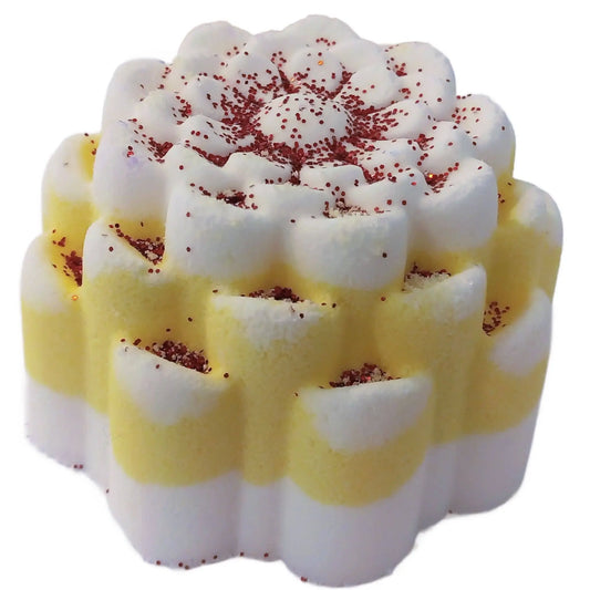 The Posh Brats Pina Colada Fizzy Bath Bomb, shaped like a flower, evokes a tropical paradise with its alternating white and yellow petals and red center sprinkles. Made from natural ingredients, it has a soft, fluffy texture.