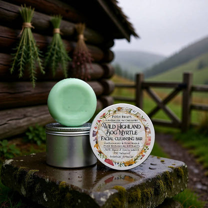 Facial cleansing bar with tin and label in front of a wooden cabin and natural landscape