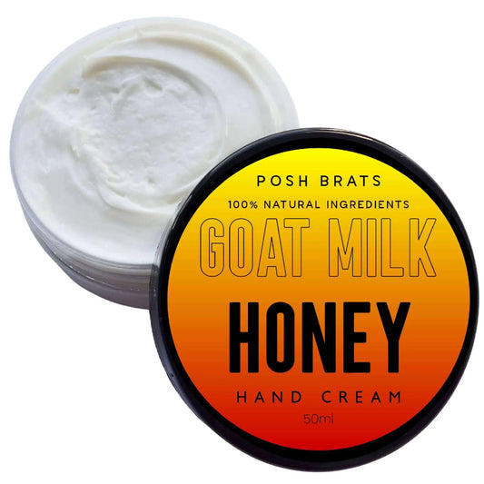 An open container of Posh Brats hand cream reveals white cream inside. The lid beside it reads 100% Natural Ingredients, Goat Milk Aloe Vera Honey Soothing Hand Cream, 50ml on a gradient orange and yellow background.