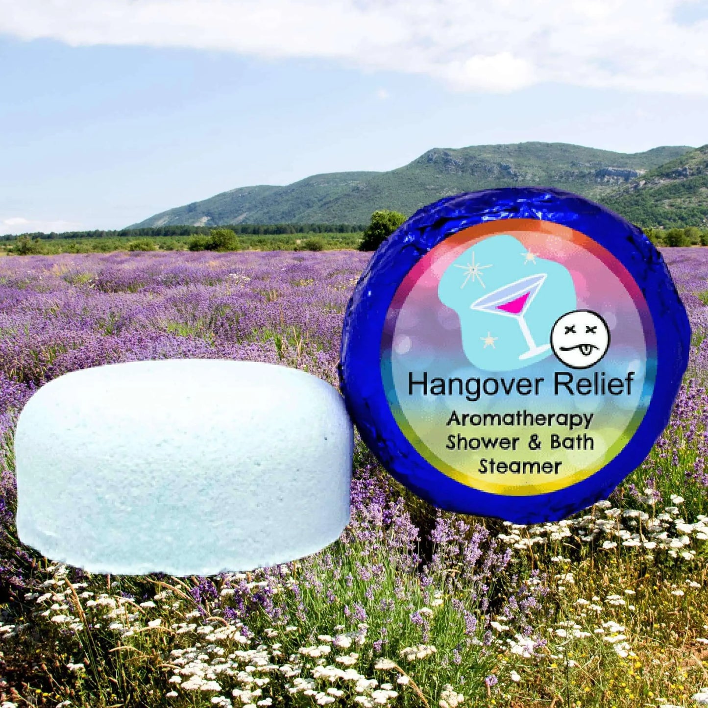 A pale blue Hangover Relief Aromatherapy Shower Steamer by Posh Brats highlights essential oils benefits against a lavender field under a blue sky. Its vibrant packaging, featuring a martini glass and sleepy face, promises soothing relief.