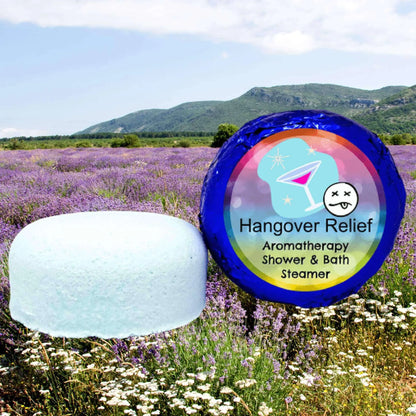 A pale blue Hangover Relief Aromatherapy Shower Steamer by Posh Brats highlights essential oils benefits against a lavender field under a blue sky. Its vibrant packaging, featuring a martini glass and sleepy face, promises soothing relief.