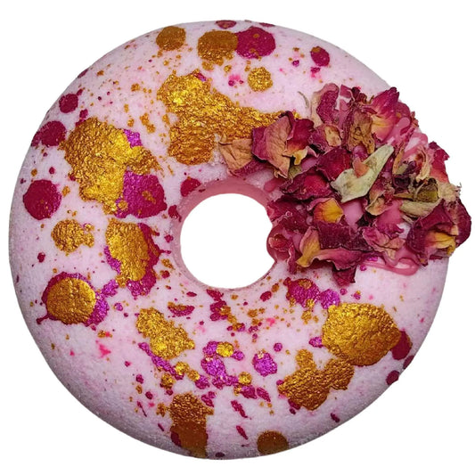 Introducing the Moonlight Kiss Donut Bath Bomb by Posh Brats, featuring a white and pink marbled design with gold and pink speckles. A small cluster of dried rose petals adorns one side, offering an aromatic journey of elegance.