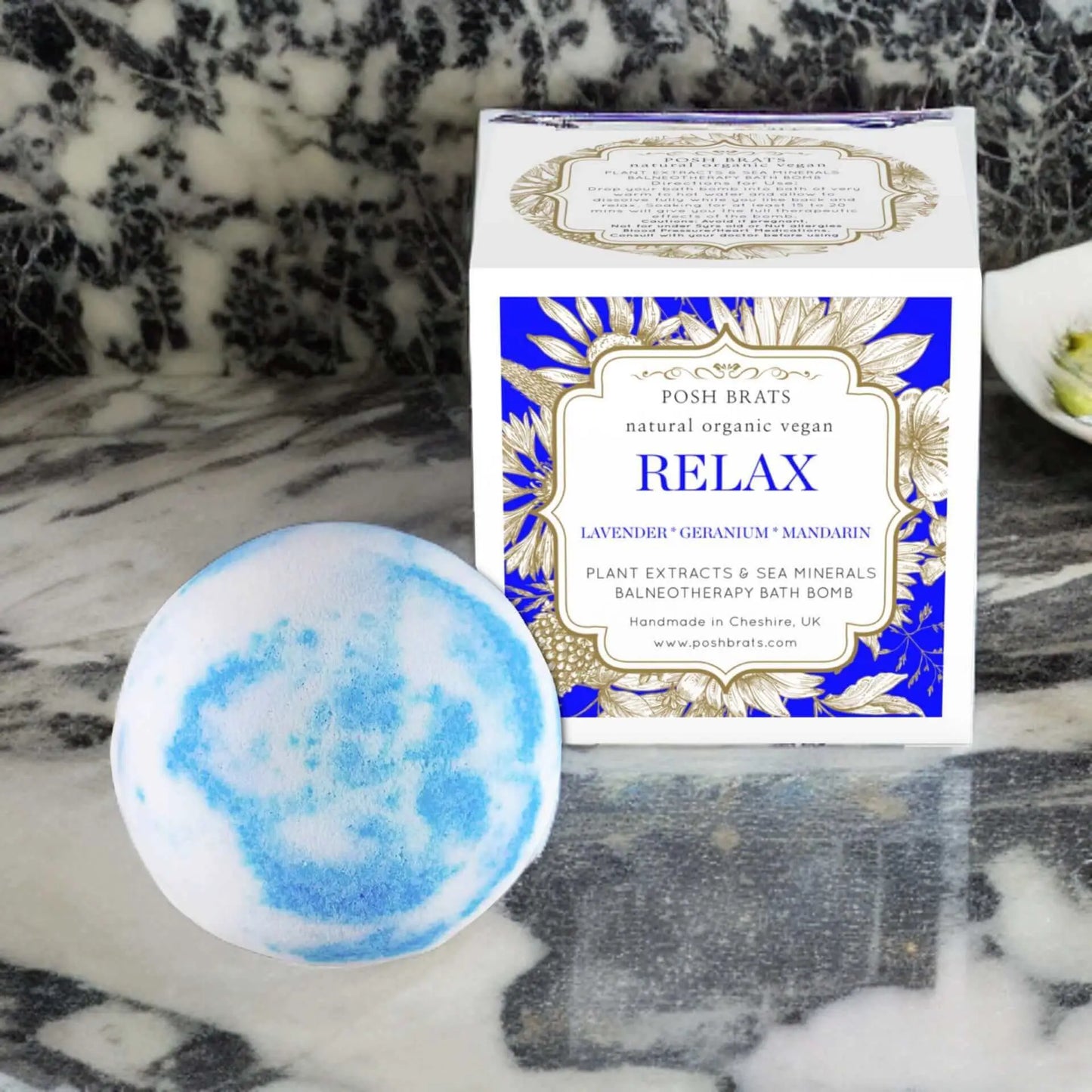 A round blue and white Relax Aromatherapy Bath Bomb in front of a square Relax box is infused with lavender, geranium, and mandarin oils for stress relief. Its vegan, organic, natural, and made by Posh Brats in Cheshire, UK.