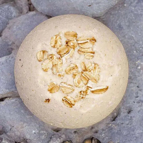 The Skin Soothing Milk Oats Unscented Fizzy Bath Bomb by Posh Brats offers a skin-soothing experience when placed on a textured stone surface.